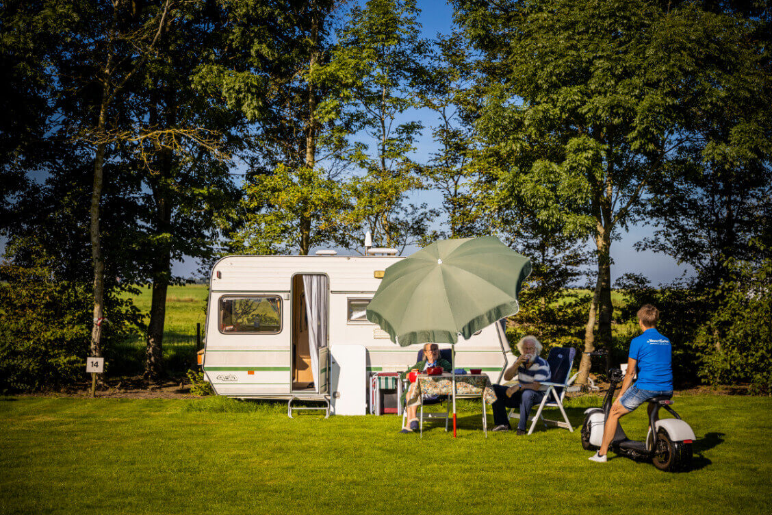 Een ruime campingplaats voor de caravan om ringt door bomen op minicamping de Wetterspetter